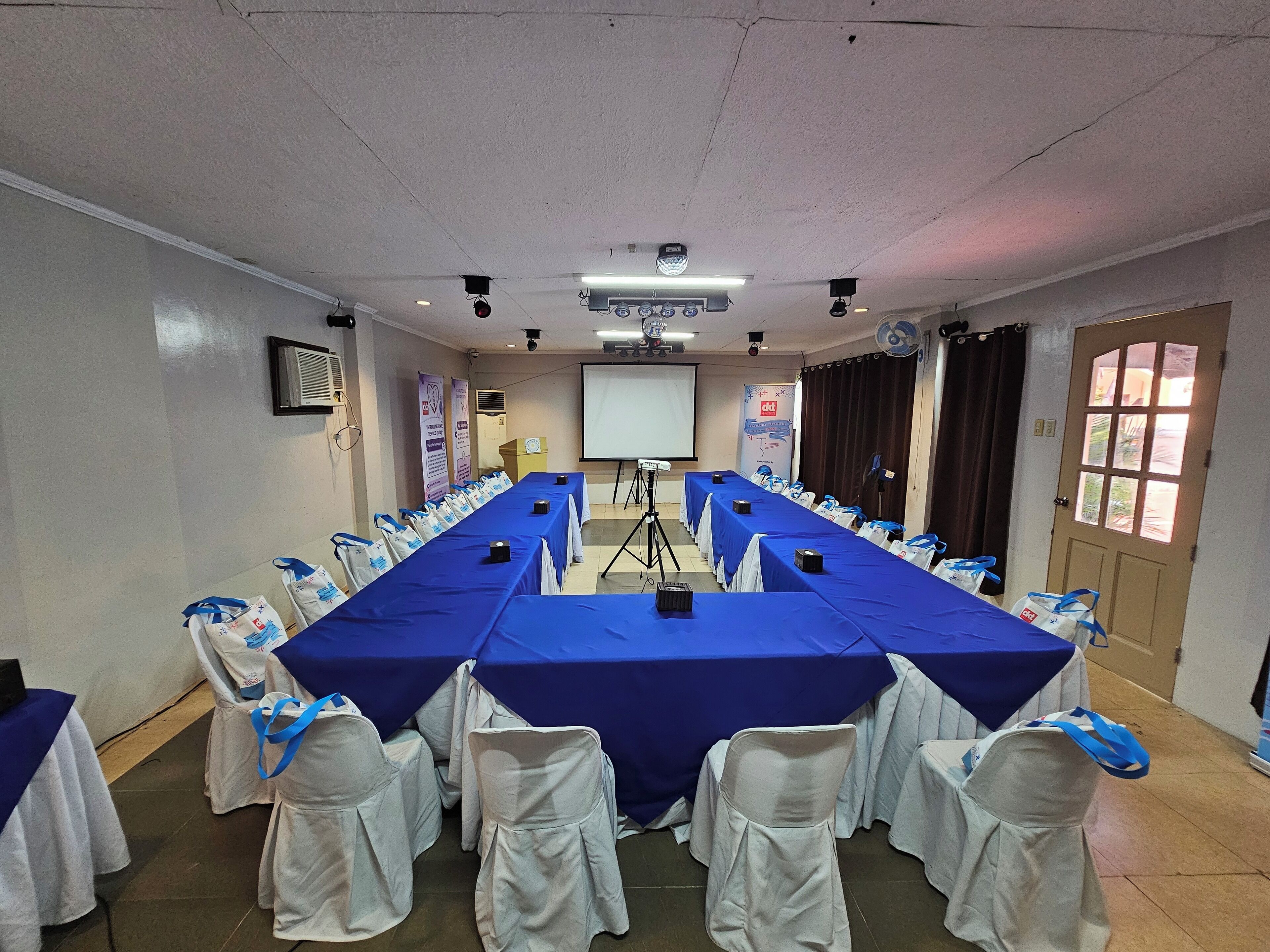 A conference room with a long table, white chairs, and a projector screen.