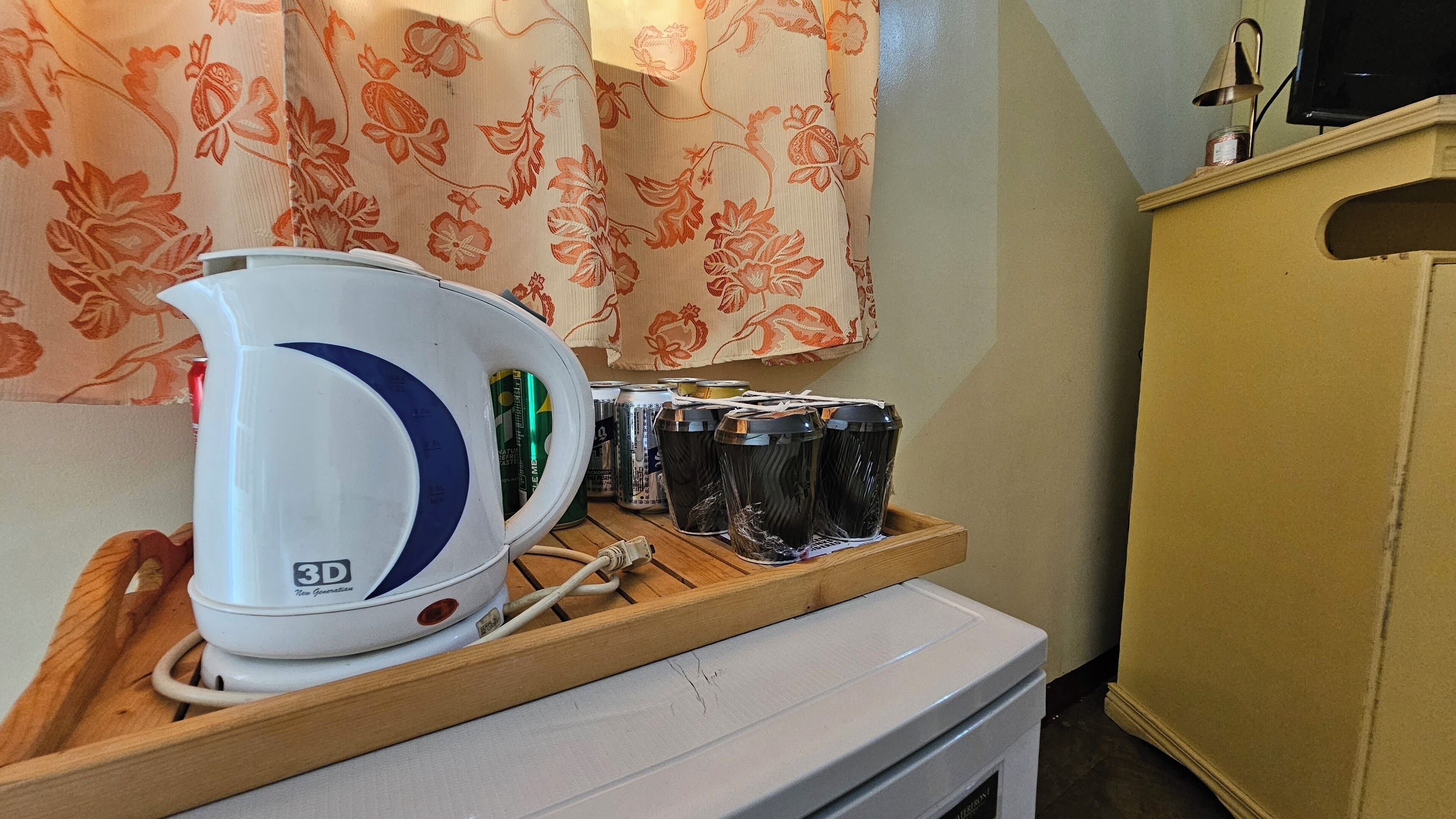 A 3D kettle on a wooden tray with several cans and glasses, a white appliance, and a yellow cabinet in a kitchen setting.