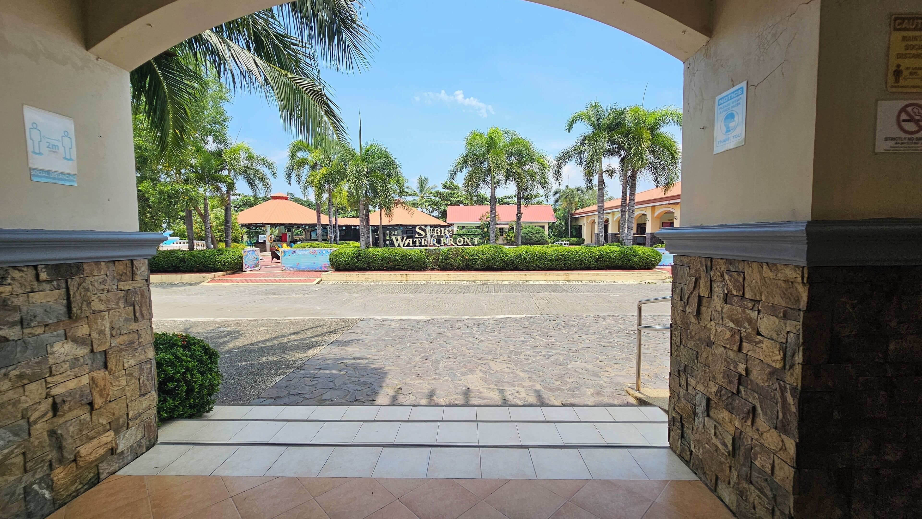 Entrada para um hotel com arco de pedra, placa com 'Subic Waterfront' e palmeiras ao fundo.
