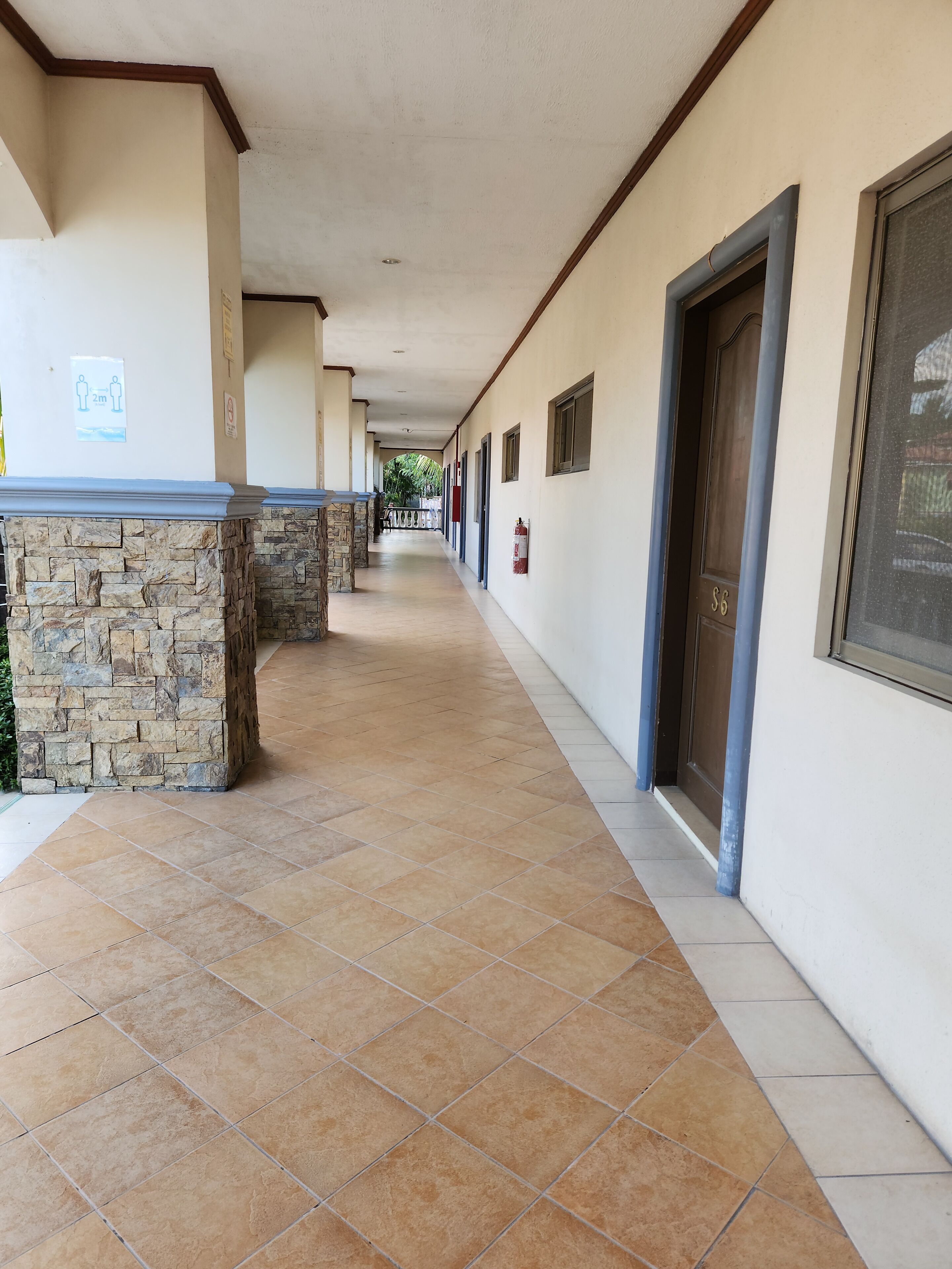 A corridor with stone pillars, tiled flooring, and doors on one side.