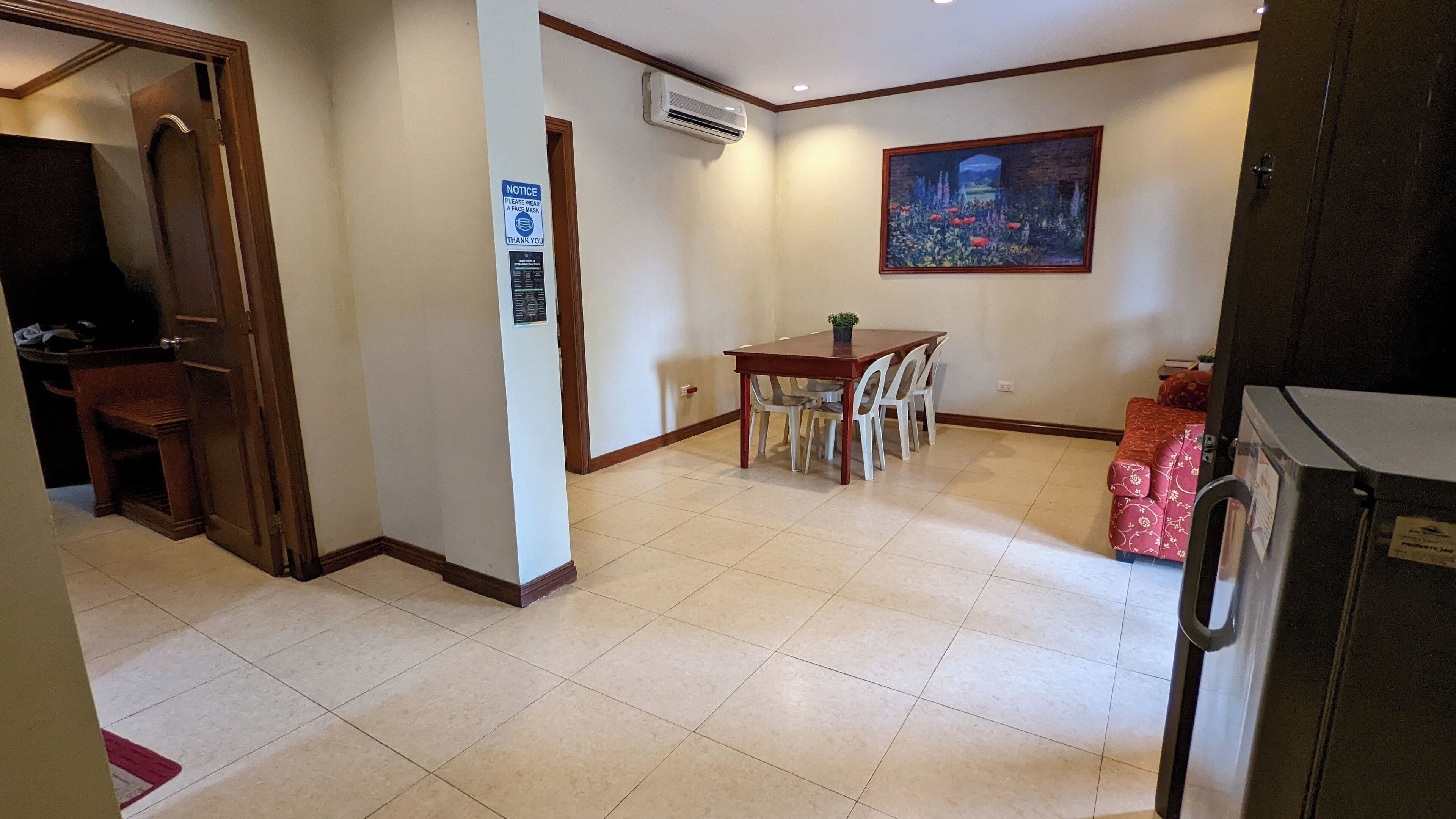 A dining area with a table and chairs, an air conditioning unit, a painting on the wall, and a refrigerator.