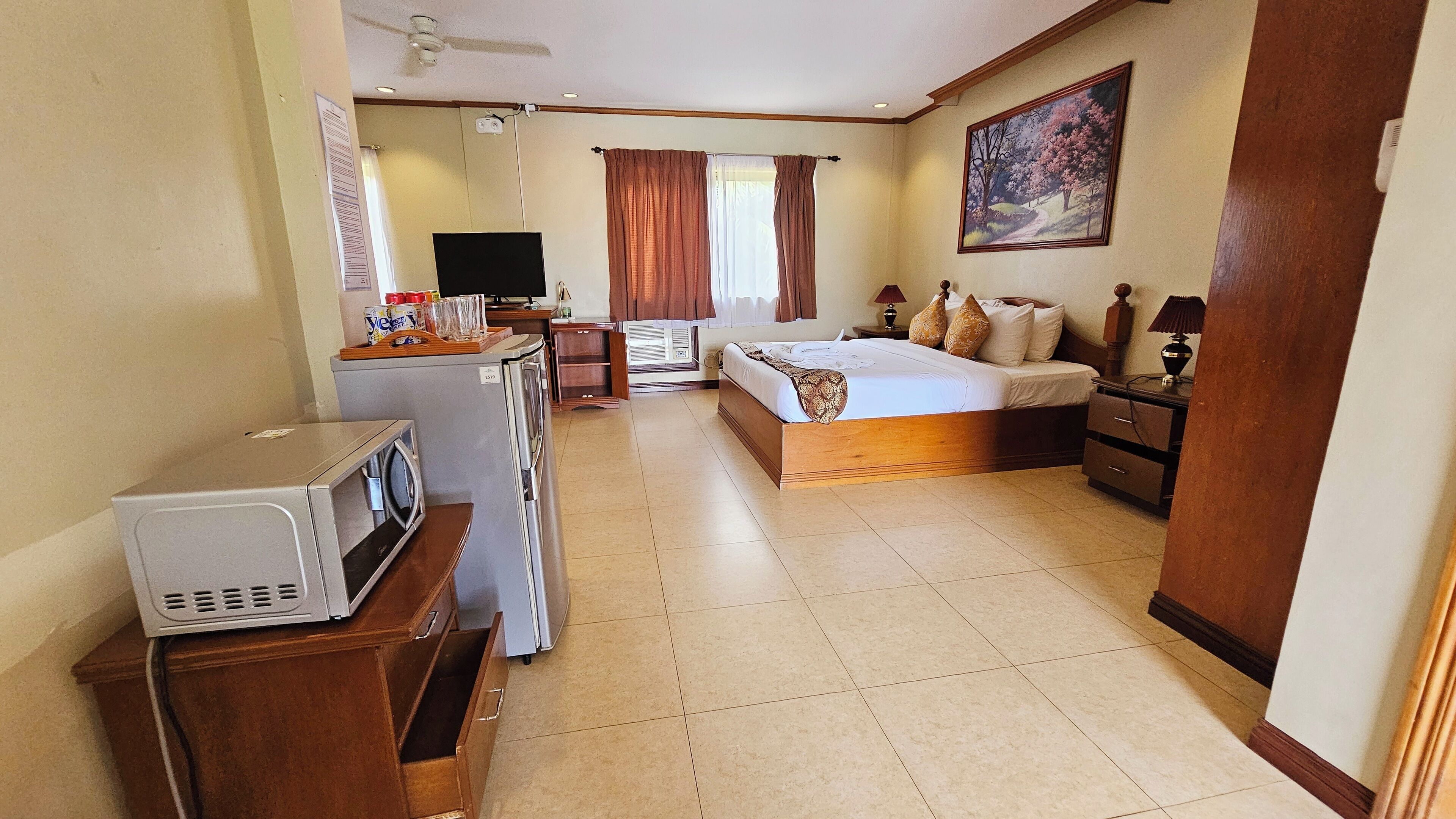 A hotel room with a bed, a desk with a computer, a washing machine, and a ceiling fan.