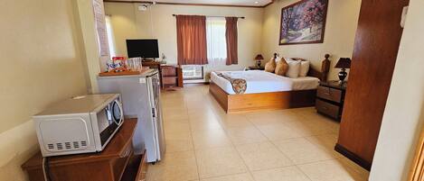 A hotel room with a bed, a desk with a computer, a washing machine, and a ceiling fan.