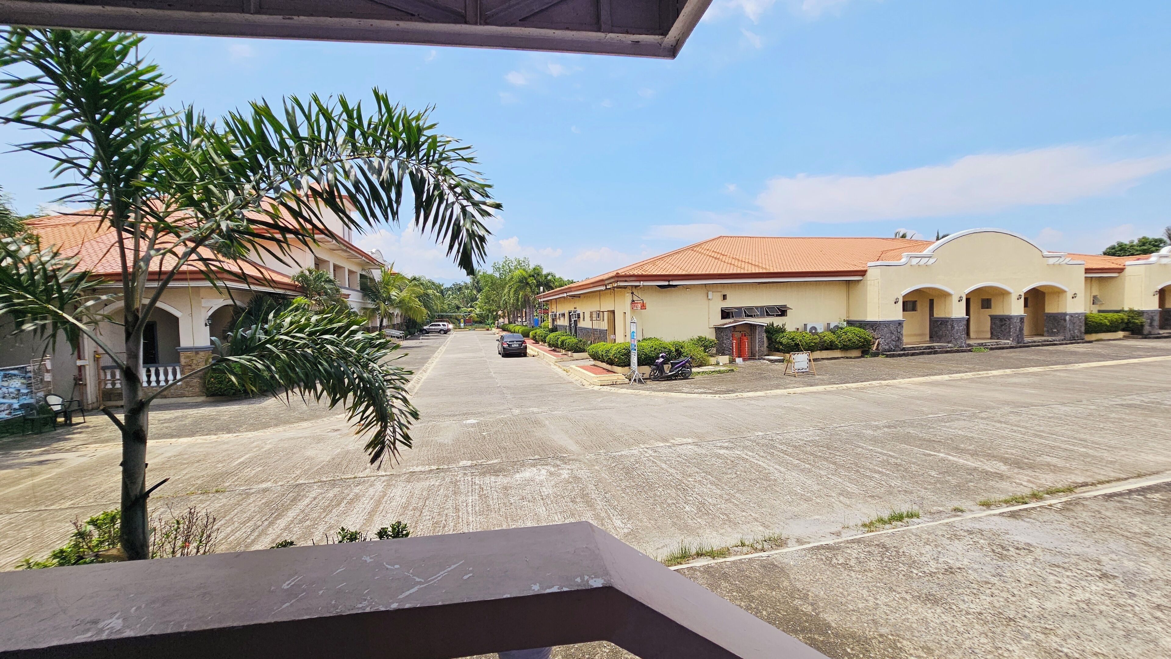 A street view of a residential area with houses featuring red-tiled roofs and a paved road.