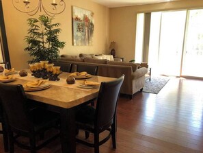 A dining area with a wooden table set for four, surrounded by dark chairs. A large potted plant is in the corner, and a painting hangs on the wall. - Tideview #85 · 3 Suites Near Convention, Universal & Disney (Orlando)