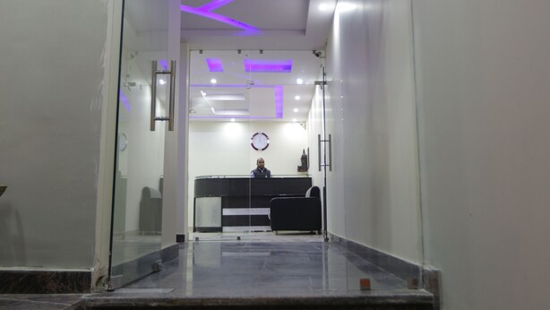 A modern hotel lobby with a reception desk, a glass partition, and a staircase leading to upper floors. - Hotel Airport International (New Delhi)