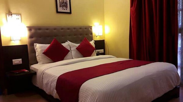 Una habitación de hotel con una cama grande, dos mesitas de noche, un cabecero y dos lámparas fijadas a la pared.