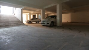 An empty parking garage with concrete floors and columns, two parked cars, and a stairway leading to an upper level. - Hotel Airport International (New Delhi)