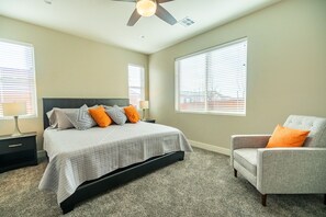 Quarto com cama, uma cadeira e duas janelas com persianas.