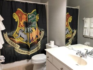 Een badkamer met douchegordijn met een draak-en-kasteel ontwerp, een toilet, een wastafel met spiegel en een handdoekhouder.