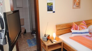 A hotel room with a bed, a bedside table with a lamp, a TV, and a small table with a remote control. - Double room no. 3 - Ferienhof Feil (Friedrichskoog)