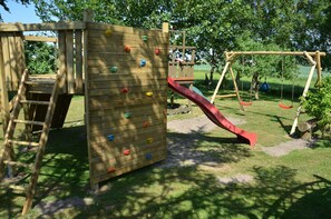 A wooden play structure with a climbing wall and a red slide.