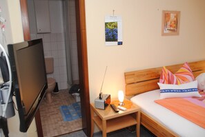 A hotel room with a bed, a bedside table with a lamp, a TV, and a small table with a remote control.