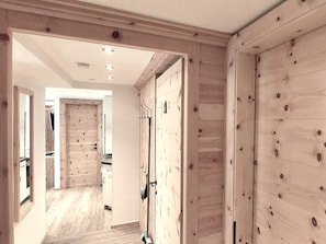 Un couloir aux murs en bois, une porte avec un porte-manteau, et un coin cuisine à l’arrière-plan.