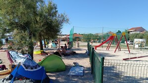 Zona de playa arenosa con tiendas de campaña, una red de voleibol y juegos infantiles.
