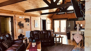 Interno accogliente di una baita di legno, con un divano in pelle, un tavolino in legno e un tavolo da pranzo rustico.