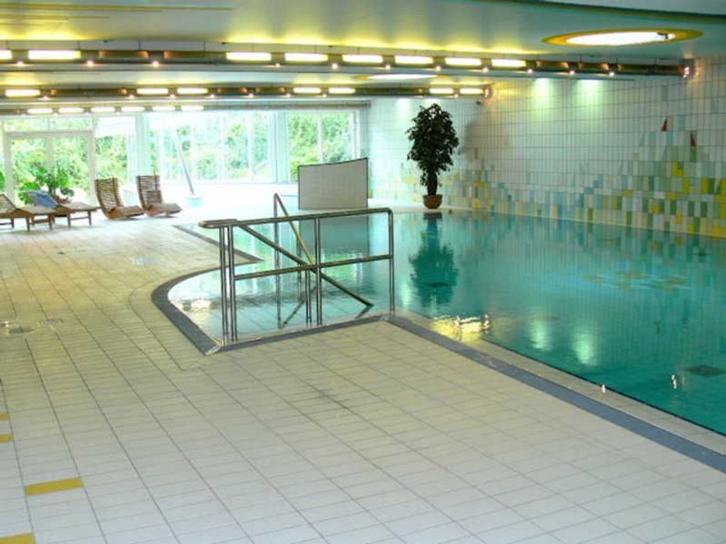 An indoor swimming pool with a tiled floor, a glass barrier, and a potted plant.
