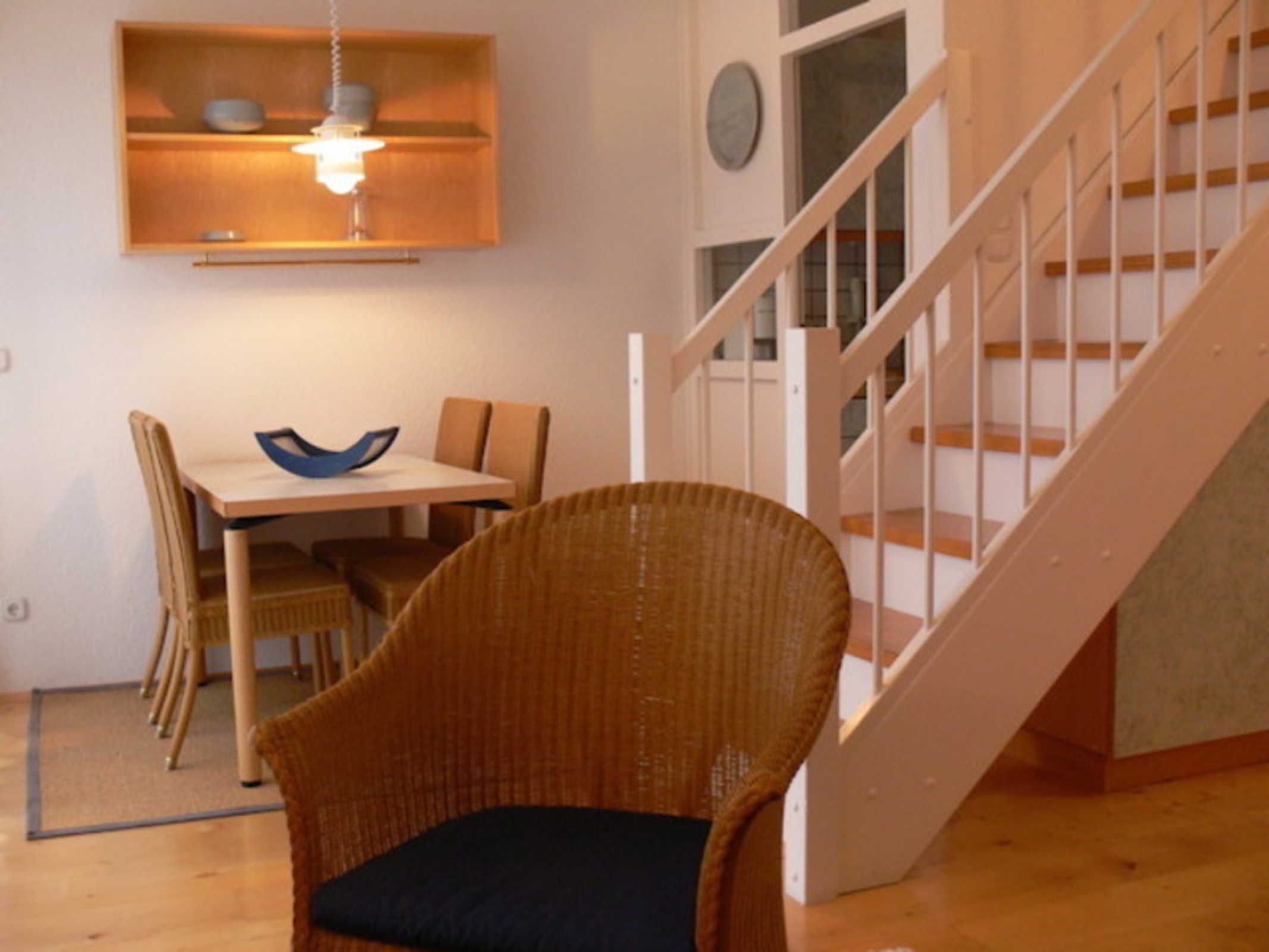 A dining area with a table, chairs, and a wicker chair with a cushion.