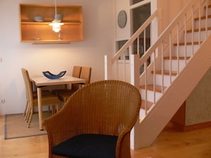 A dining area with a table, chairs, and a wicker chair with a cushion. - Apartment (2) - Apartments in Kloster (Insel Hiddensee)