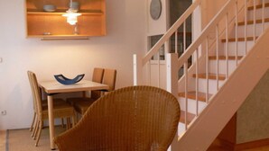 A dining area with a table, chairs, and a wicker chair with a cushion. - Apartment (2+2) - Apartments in Kloster (Insel Hiddensee)