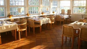 A dining area with multiple tables and chairs, large windows, and a tiled floor. - Apartment (2+2) - Apartments in Kloster (Insel Hiddensee)