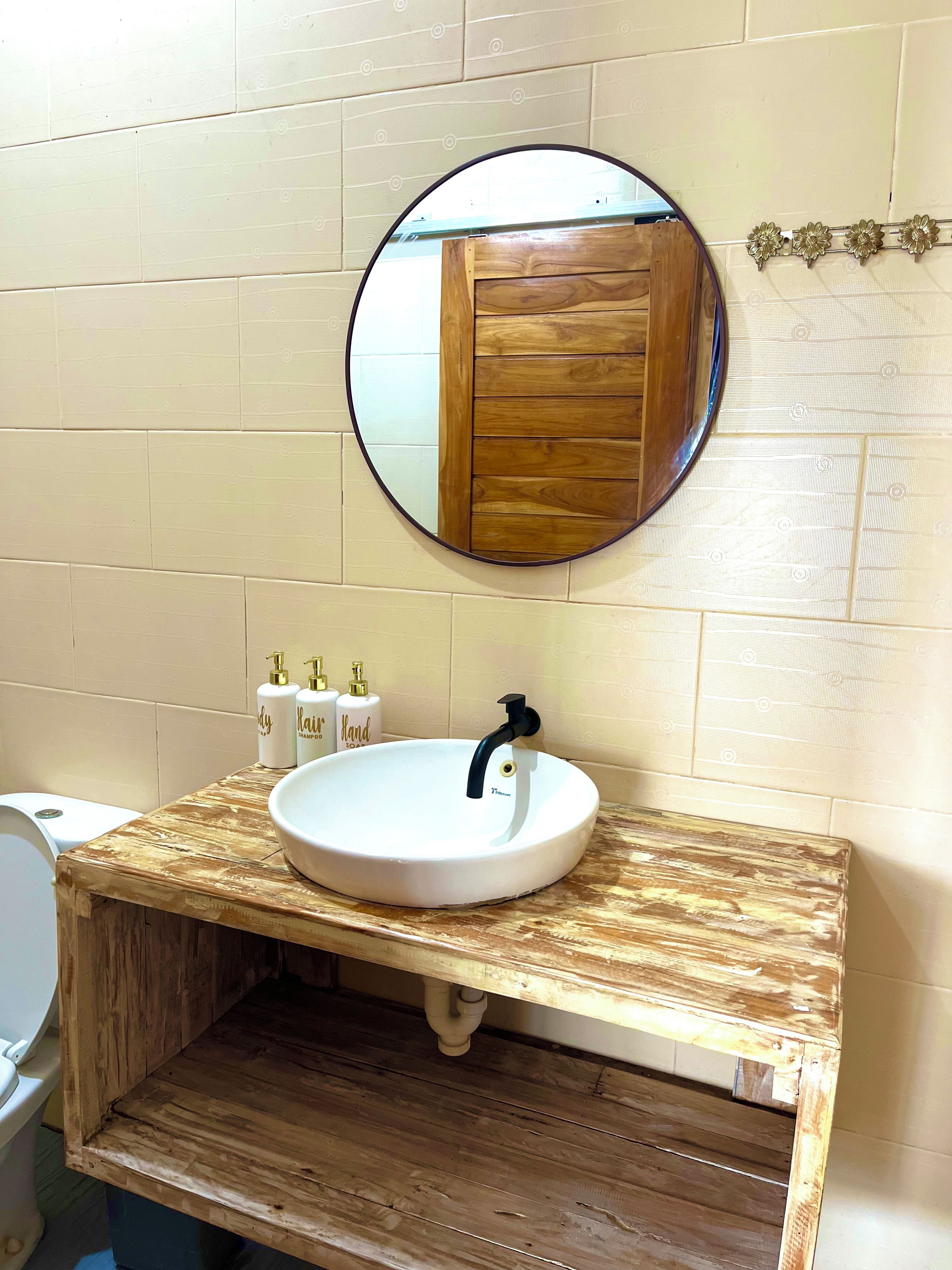 A bathroom with a round mirror, a white sink, and wooden vanity.