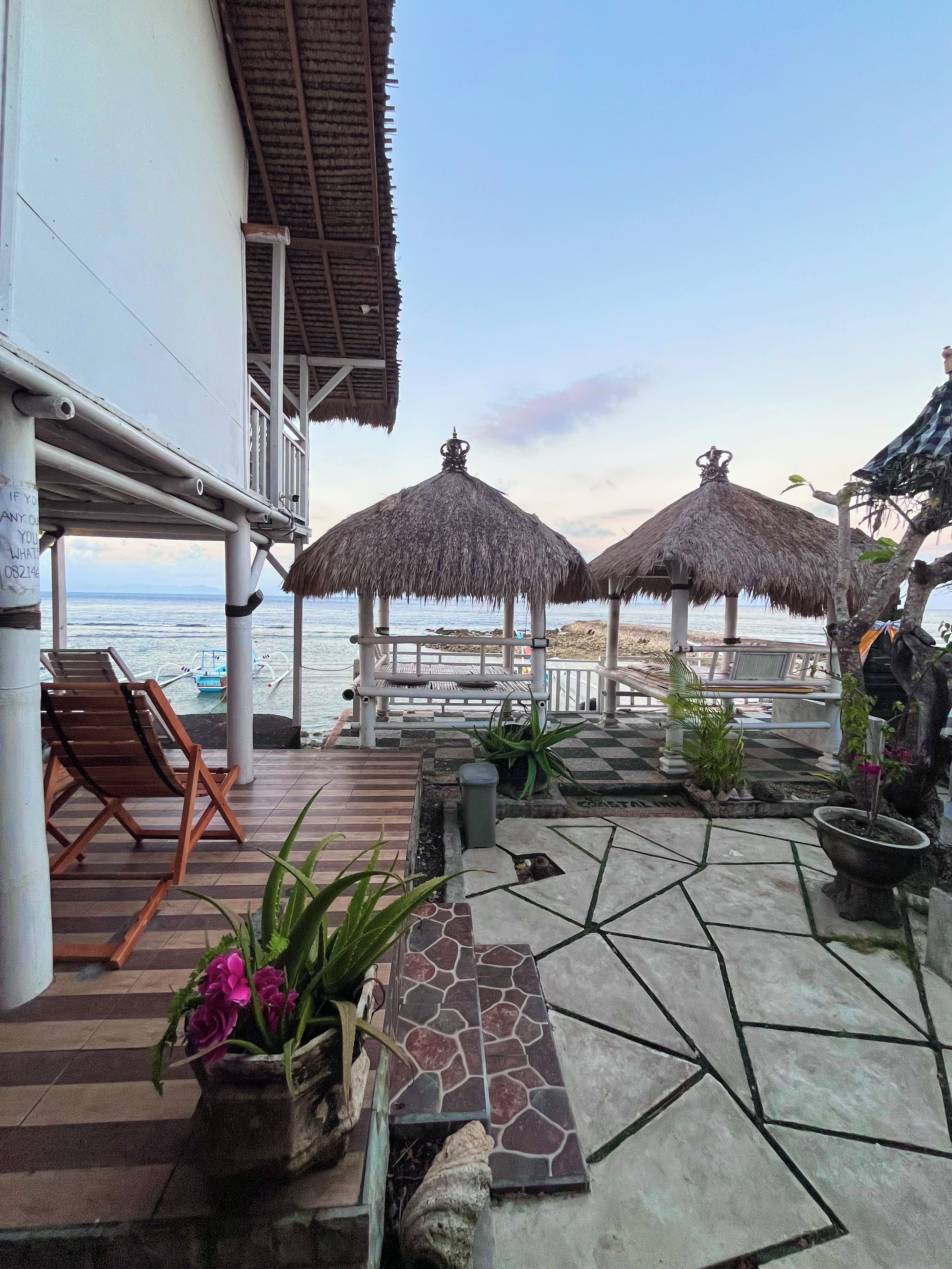 A beachside patio with thatched umbrellas, lounge chairs, and potted plants.