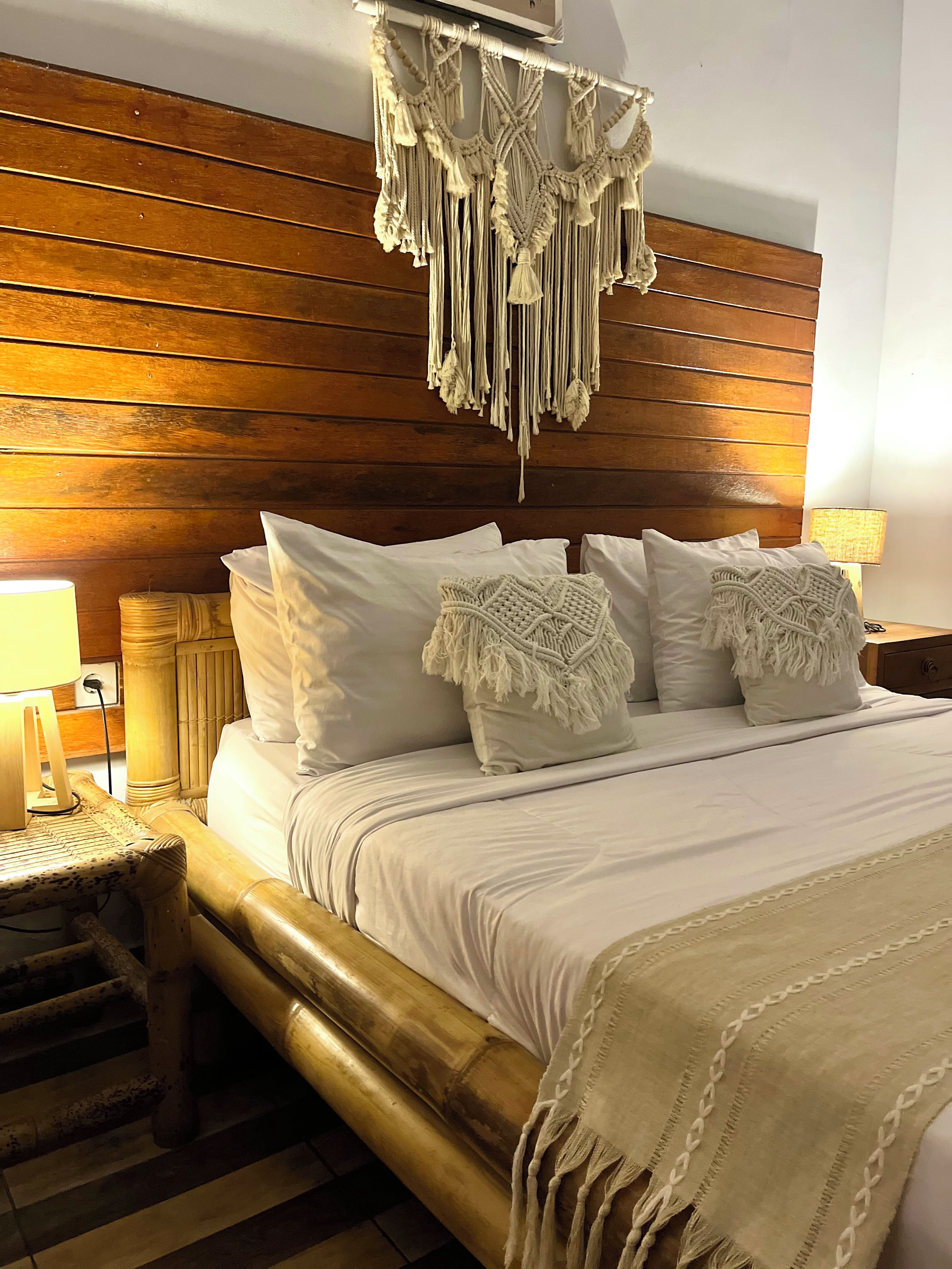 A bed with white bedding, a macrame headboard, and a bedside lamp.