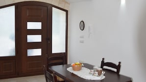 Un coin repas avec une table et des chaises en bois, un panier de fruits et un luminaire fixé au mur.