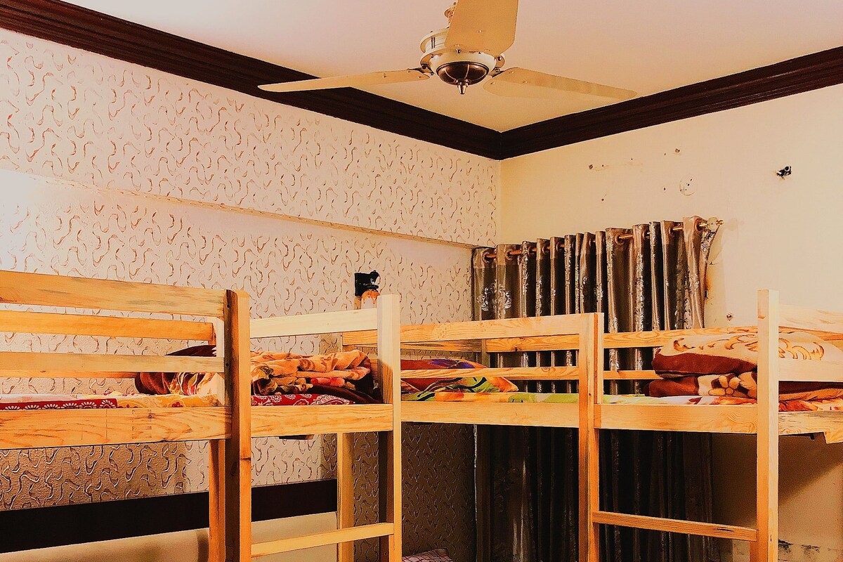 A bunk bed room with a ceiling fan, patterned wallpaper, and a window with curtains.