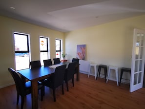 Zona pranzo con tavolo e sedie in legno, ampie finestre, un termosifone e una porta.