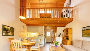 Un vaste espace de vie avec un balcon en bois, une table à manger avec des chaises, un canapé et une cuisine en arrière-plan.