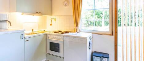 A compact kitchen with white cabinets, a stove, a dishwasher, and a window with curtains.