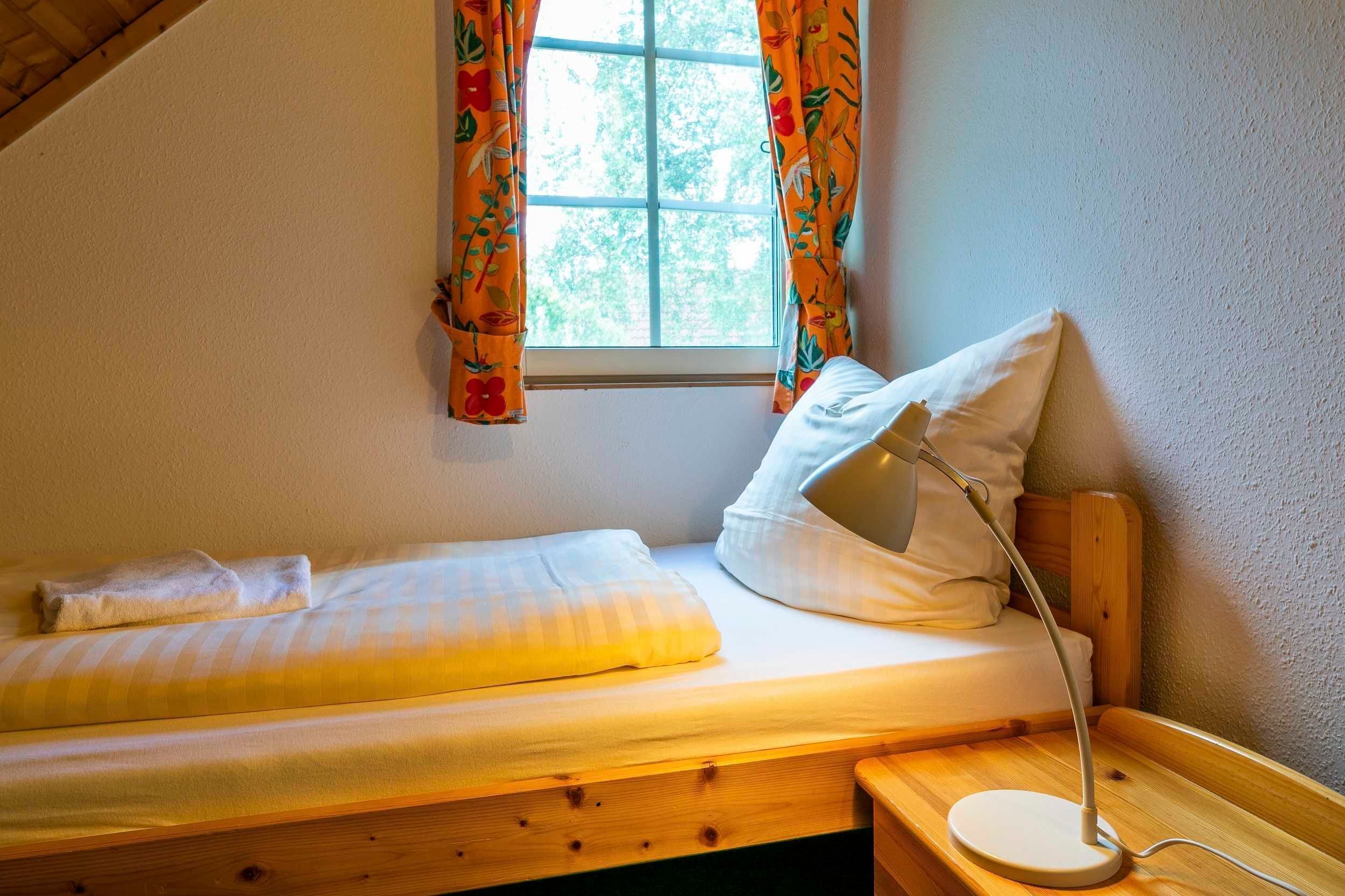 A small, cozy room with a single bed, a bedside table, and a window with curtains.