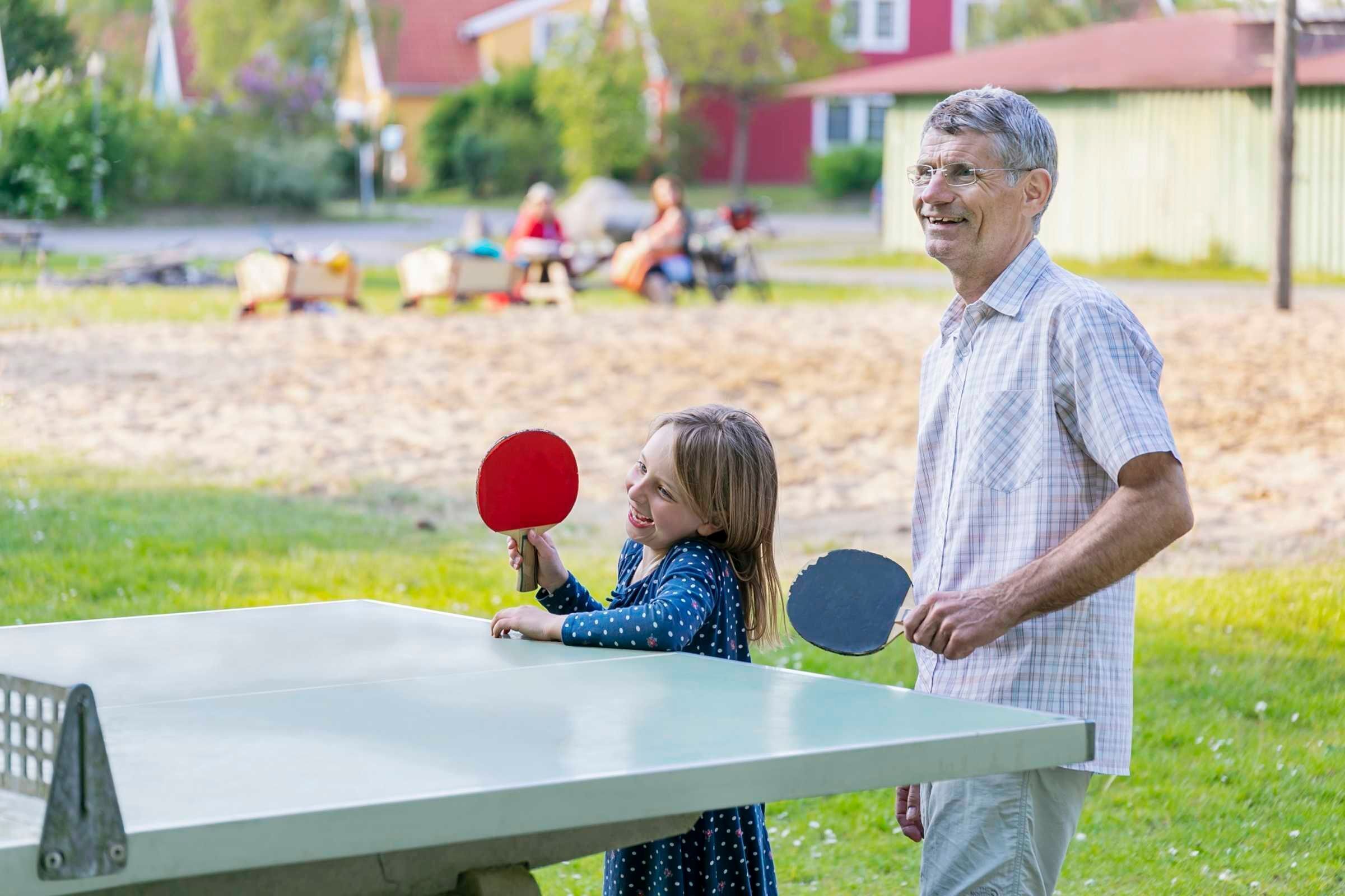 A table tennis table in an outdoor setting with a grassy area and a few people in the background.