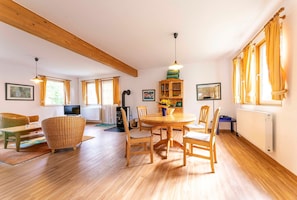 Ein gemütliches Wohnzimmer mit einem Holzesstisch, Stühlen und einer Couch. Ein Fernseher, ein Schrank und eine Heizung sind ebenfalls vorhanden.