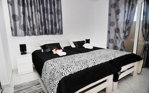 Un dormitorio moderno con una cama grande, cabecera blanca y cortinas grises.