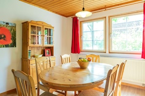 A dining area with a wooden table and chairs, a wooden cabinet with glass doors, and a window with red curtains. - Semi-detached house Storch, 6 persons, 80 sqm, GS, fireplace (18) - Holiday village (Rechlin)