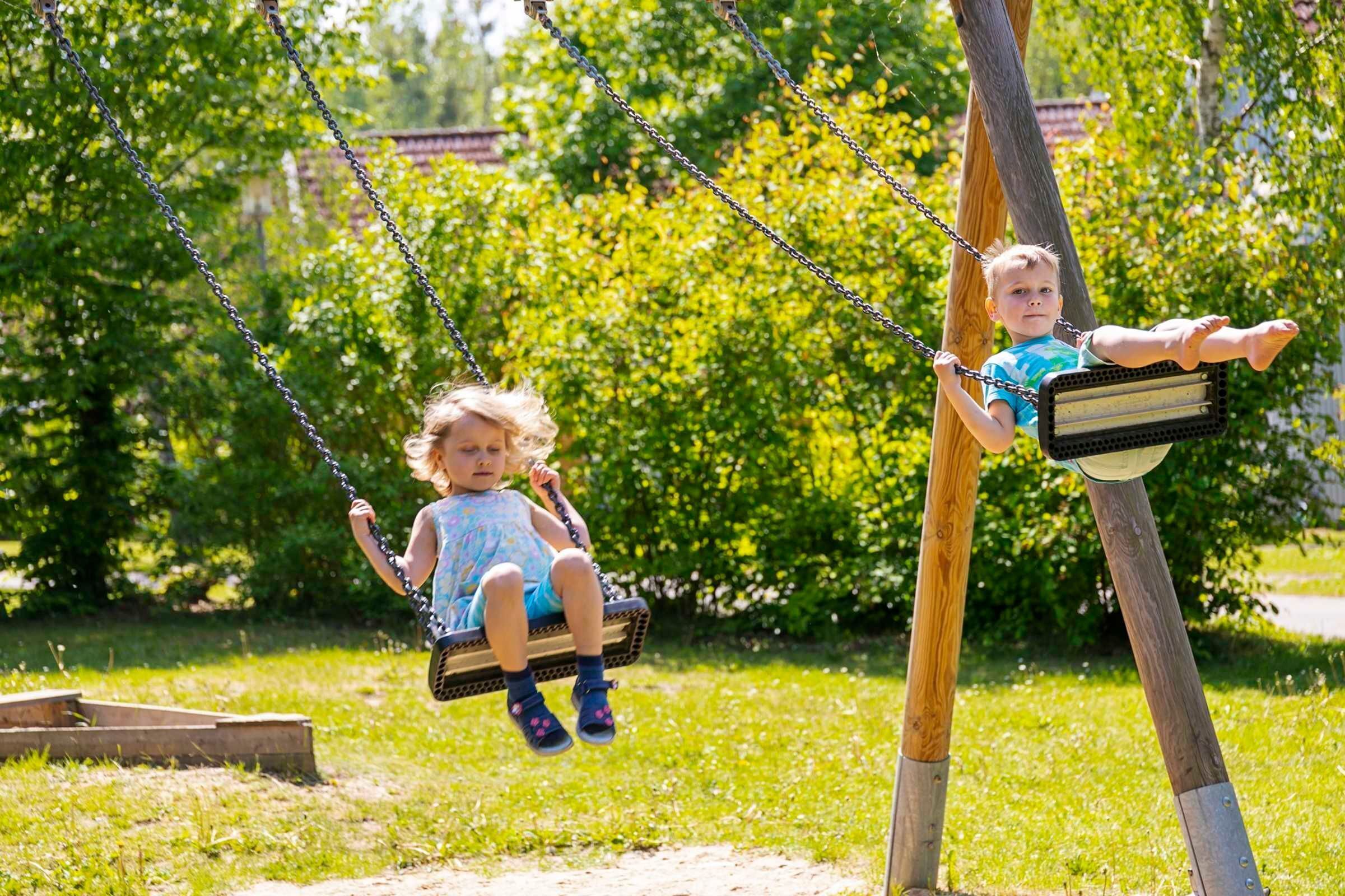 Two children on swings in a park with greenery in the background.