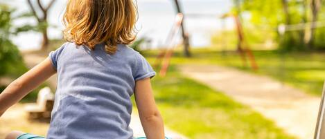 A child sitting outdoors with a view of a park and trees.