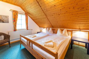 Une chambre avec un plafond en bois incliné, un lit avec du linge de lit blanc, une chaise et une fenêtre avec des rideaux.