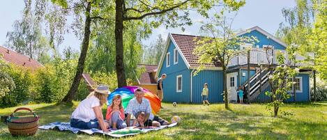 A family enjoying a picnic on a blanket in a grassy area with a blue house in the background.