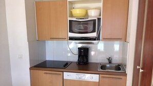 Una cocina compacta con armarios de madera, microondas, cafetera y lavavajillas.