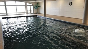 Una piscina interior con agua cristalina, un reloj en la pared y una planta en maceta.