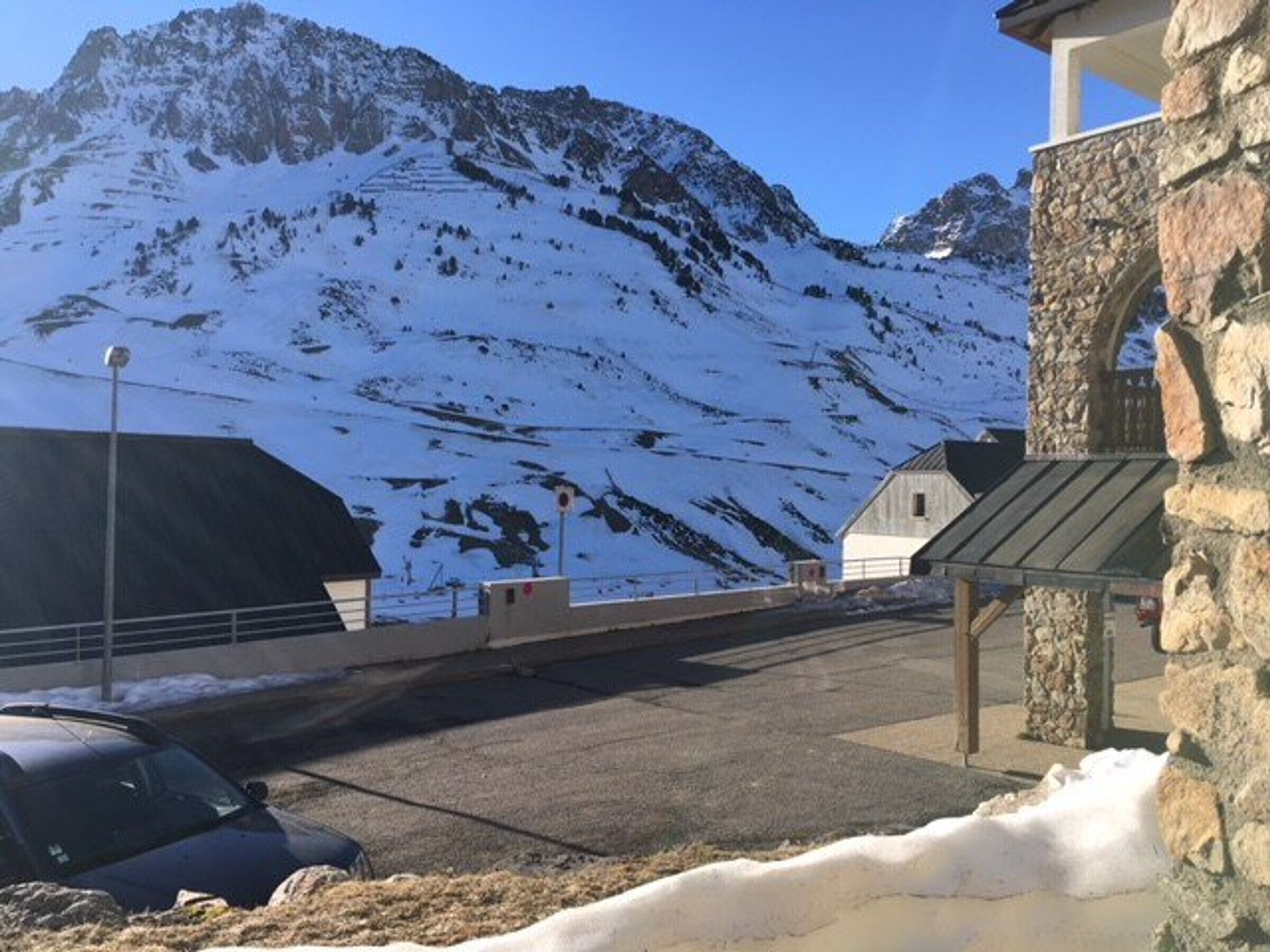 Une montagne enneigée, avec un bâtiment en pierre et une voiture garée devant.