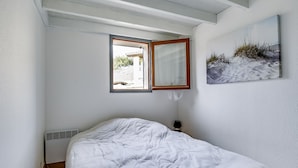 Ein Schlafzimmer mit einem Bett, einem Fenster, einem Wandspiegel und einem Gemälde.