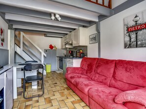 A compact living space with a kitchenette, a red sofa, a dining area, and a staircase leading to an upper level.