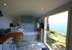 A bedroom with a bed, a desk, a chair, and a view of the sea.