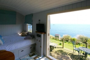 Enjoy a sea view from the comfort of your room, featuring a large bed, a table and chair by the window, and a balcony with a table and chairs.