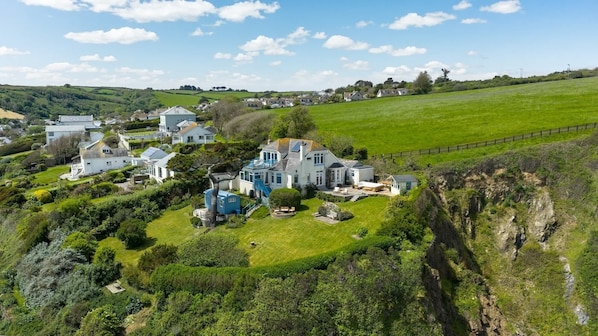 A large estate with multiple buildings, expansive green fields, and a cliffside.